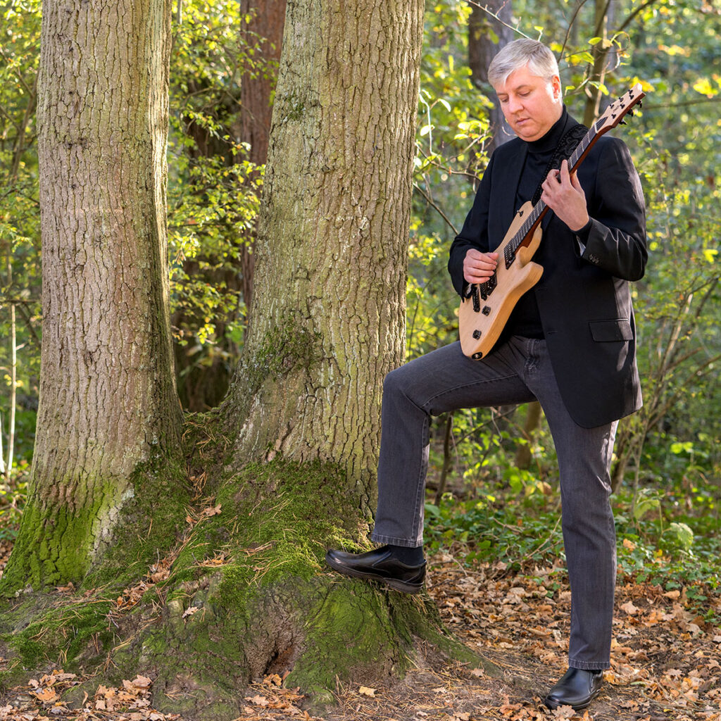 Foto von Gitarrist Alex Litau in ganzer Ansicht im sonnenbeschienenen Wald stehend